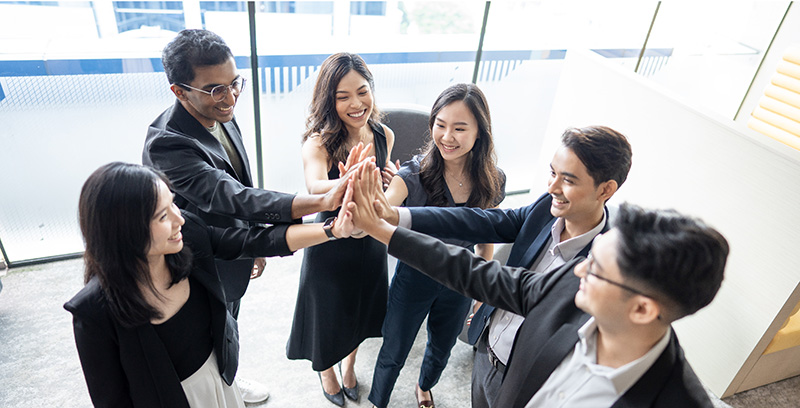 Group of young professionals in business attire high-fiving in a bright office space.